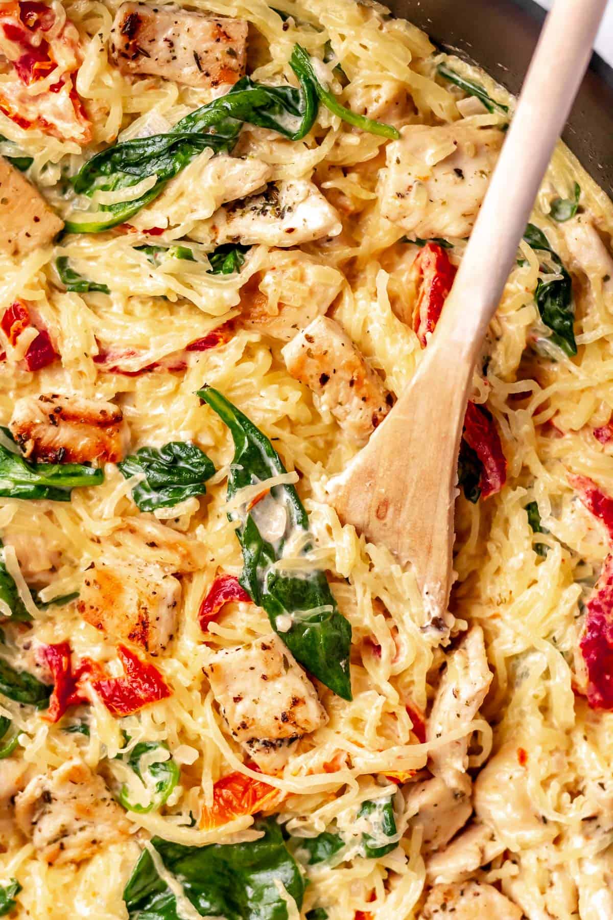 Close up of Tuscan chicken and spaghetti squash with a wood spoon in it.