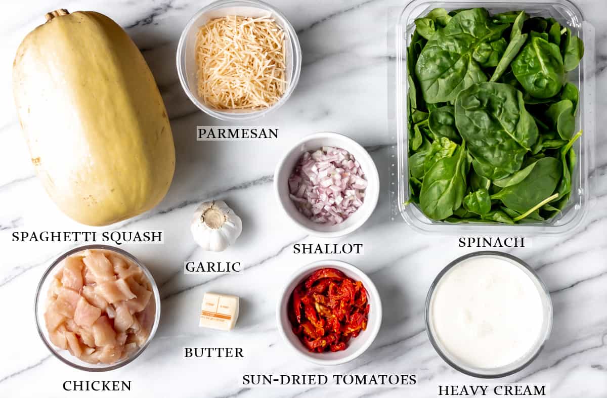 Ingredients to make Tuscan chicken and spaghetti squash on a marble background with text overlay.