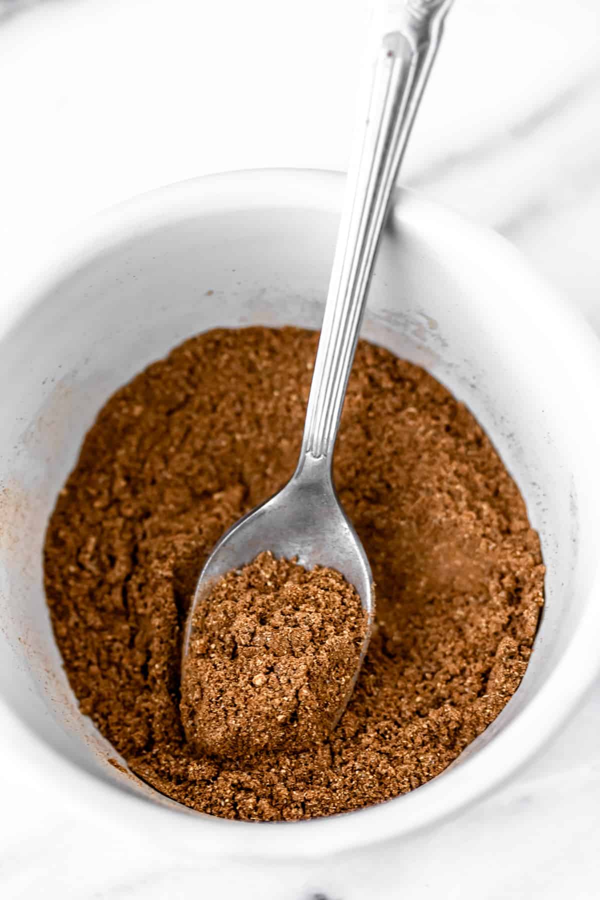 Chai spice mix in a small white bowl with a small silver spoon.