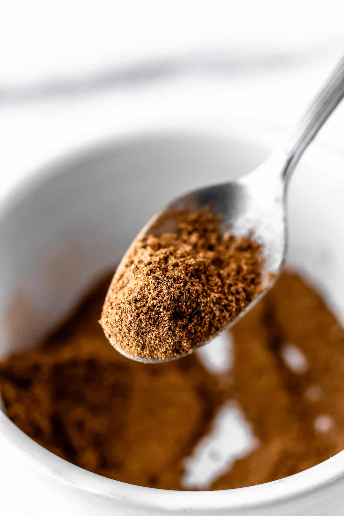Close up of chai spice mixture on a spoon over a white bowl.