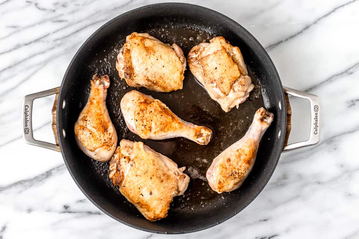 Chicken legs and thighs cooking in a black skillet.