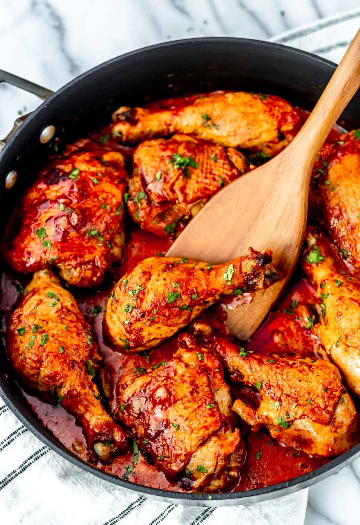 Chicken Paprikash in a black skillet with a wood turner lifting up a leg and a striped towel underneath.