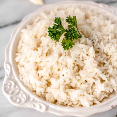 Close up of garlic rice in a white bowl with parsley on top.