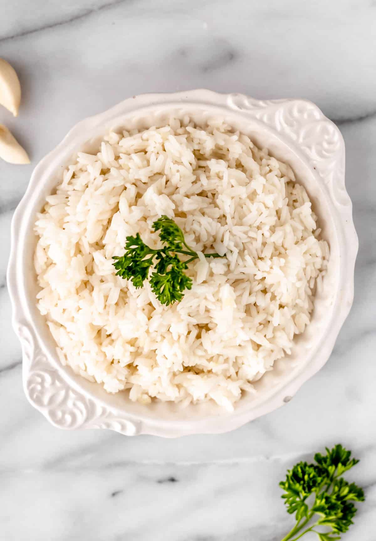 Overhead of garlic rice in a white bowl with parsley on top and extra parsley and garlic around the bowl.
