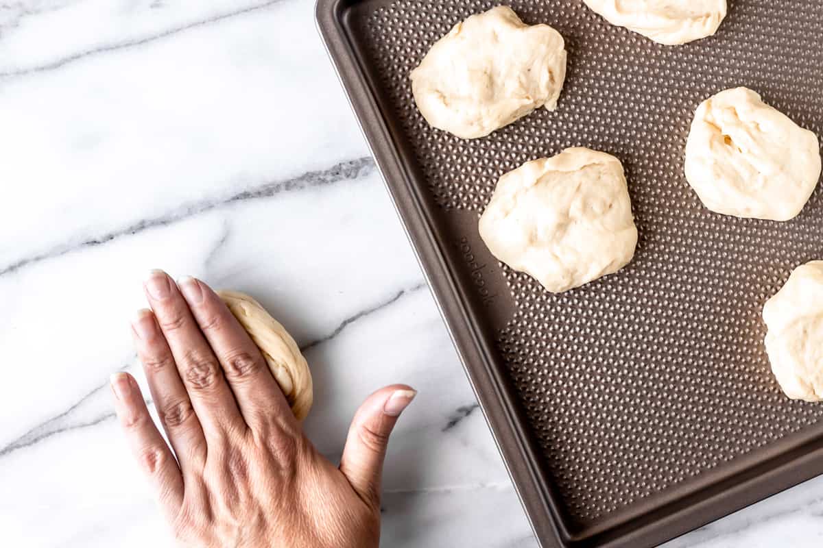 Shaping dinner rolls with a tray of dough pieces and a hand rolling the dough.