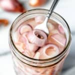 Close up of pickled shallots in a mason jar with a small fork lifting some up.