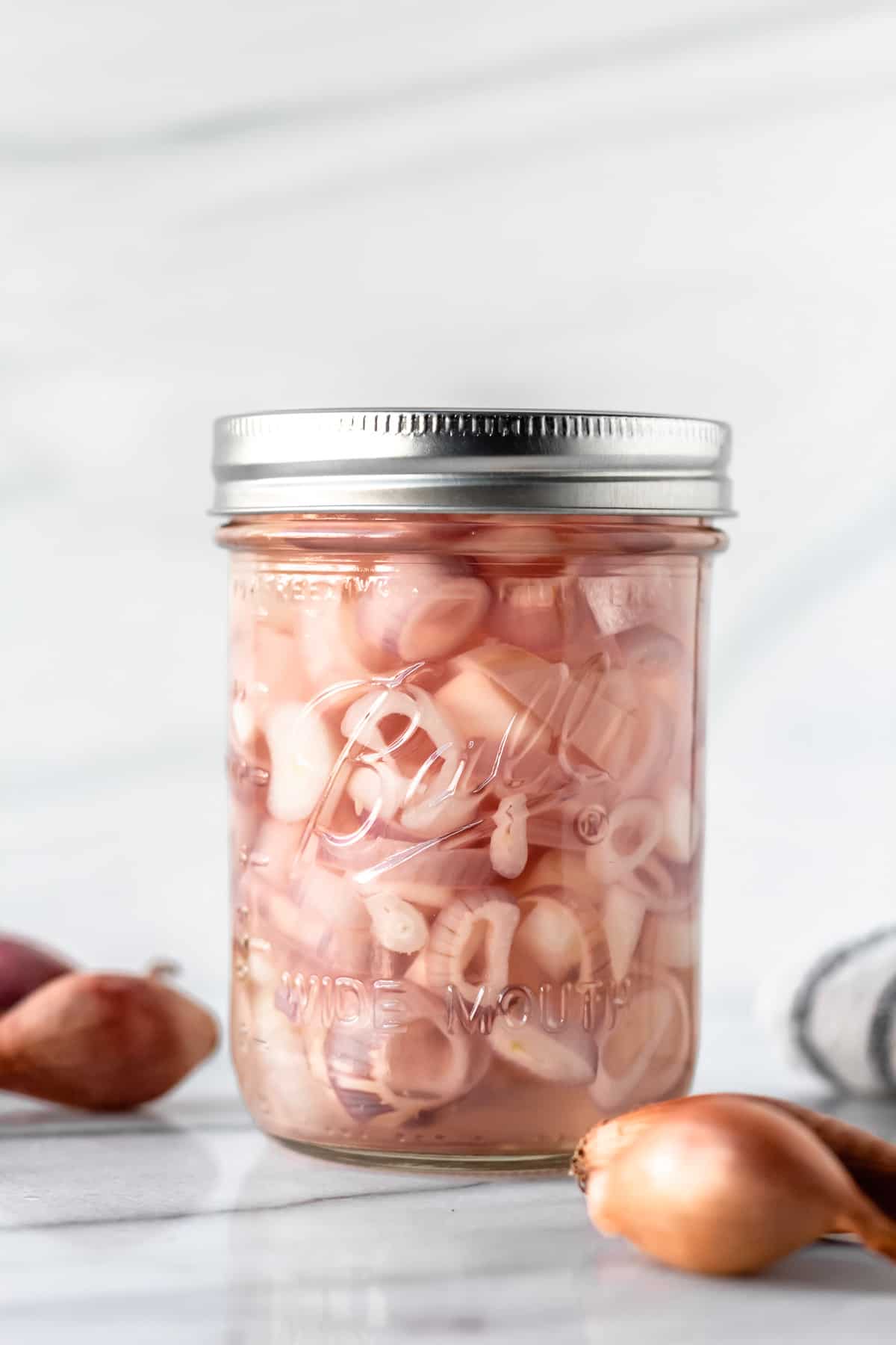 Pickled shallots in a jar with a lid and whole shallots around the jar.