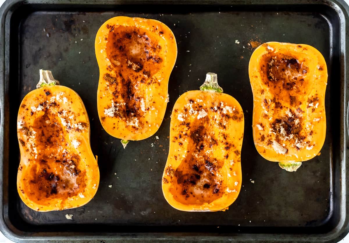 Raw honeynut squash on a baking sheet with brown sugar and cinnamon on them.