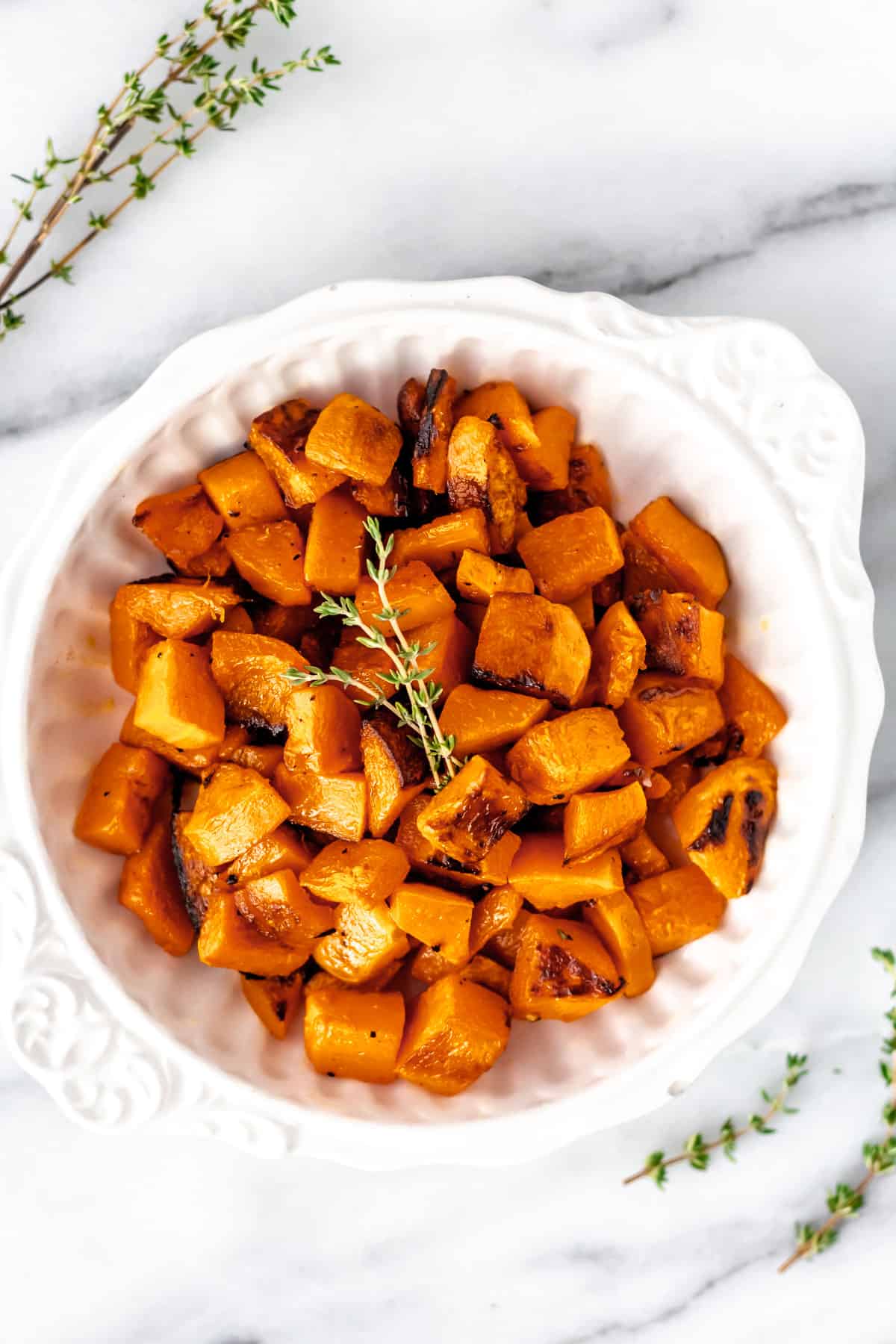Overhead of roasted honeynut squash with thyme on top of it and around the bowl.