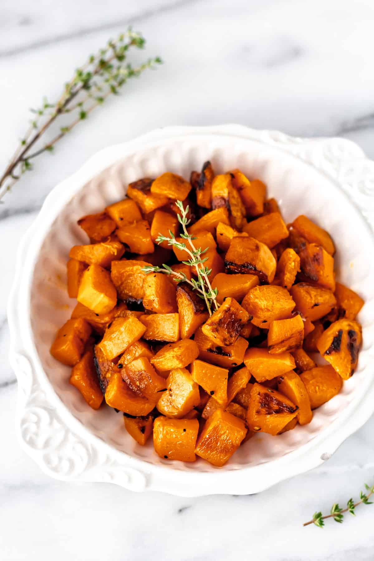 Close up of roasted honeynut squash in a white bowl with fresh thyme garnish on it and around the bowl.