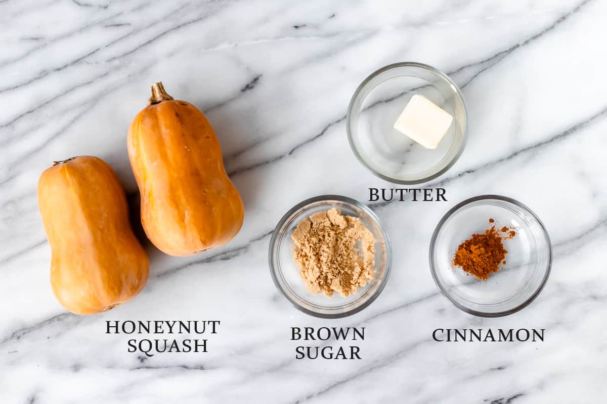 Ingredients to make roasted honeynut squash on a marble backdrop with text overlay.