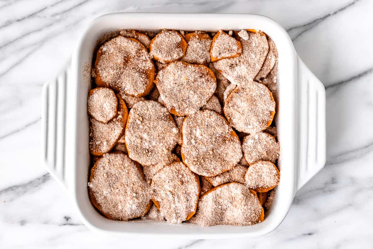 Sweet potatoes in a casserole dish with sugar and spices sprinkled on top.