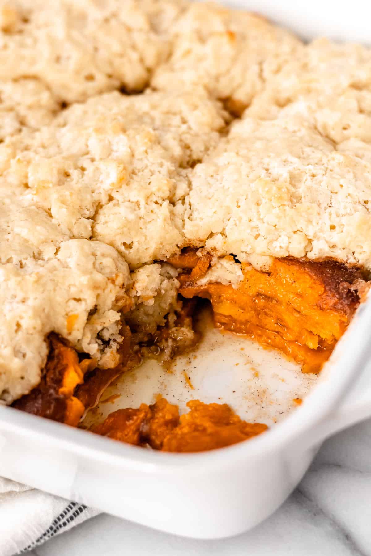 A sweet potato cobbler in a baking dish with a serving removed showing the layers of sweet potatoes inside.