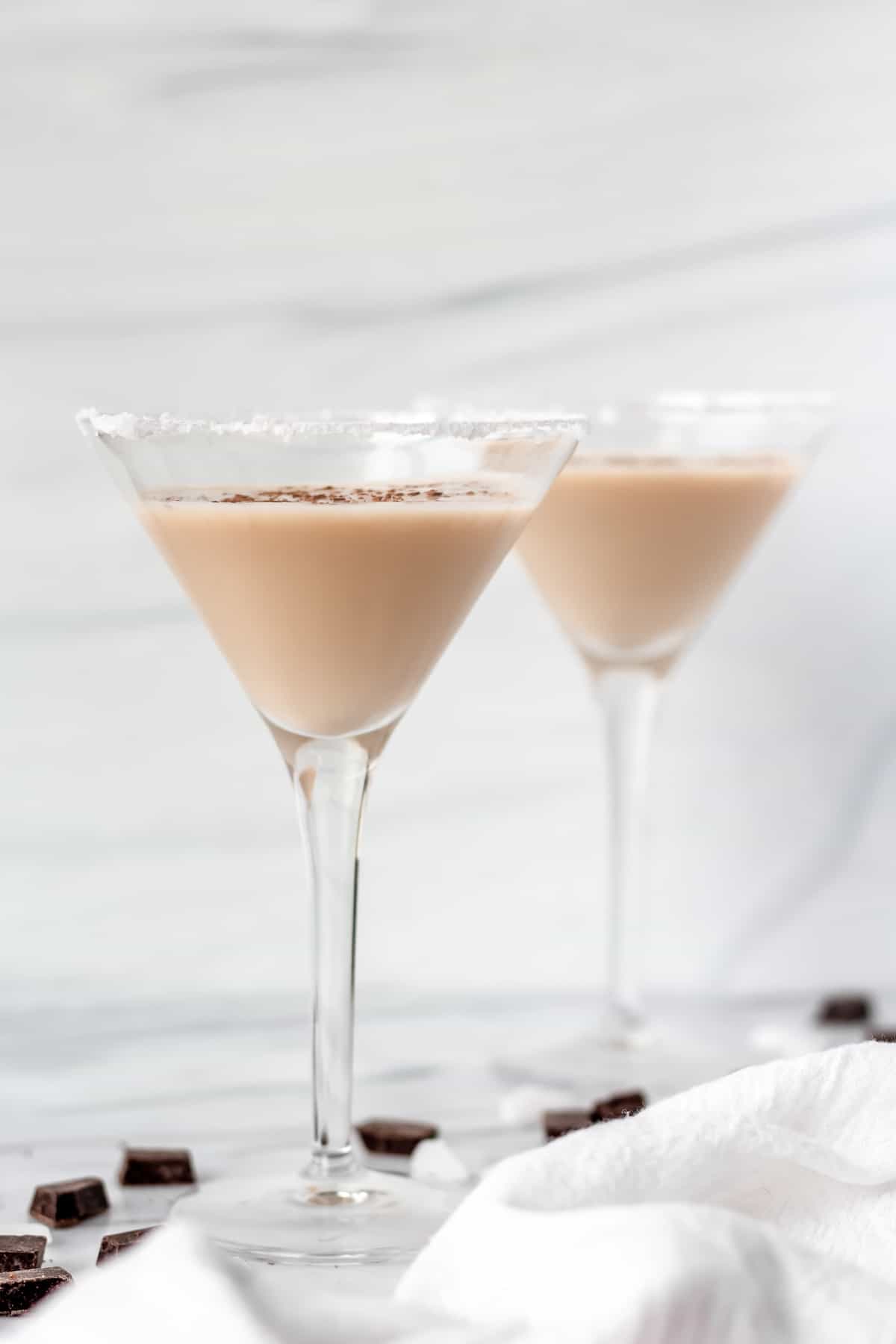 2 chocolate mint martinis from the side with a white towel and chocolate pieces.
