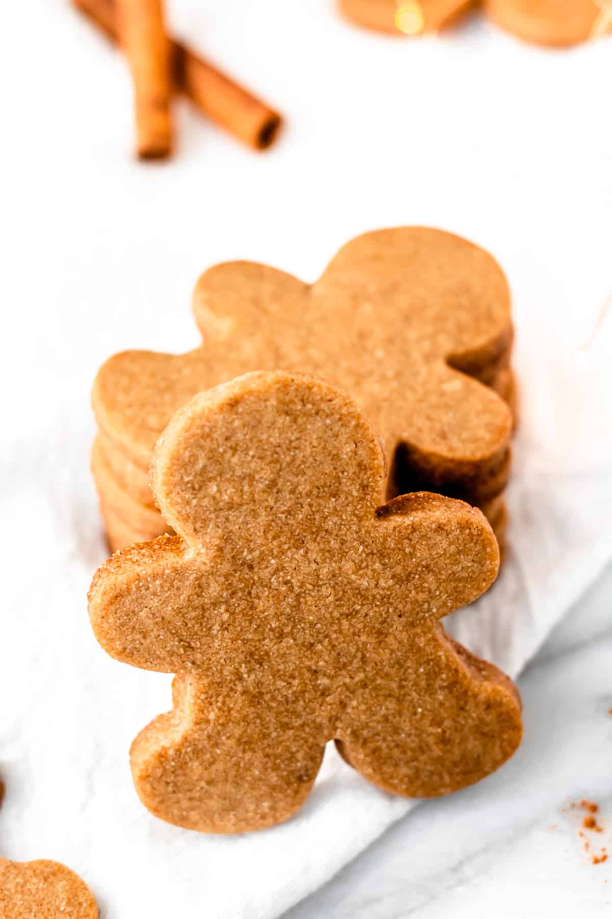 A stack of gingerbread cookies with one propped upright on the stack and cinnamon sticks in the background.
