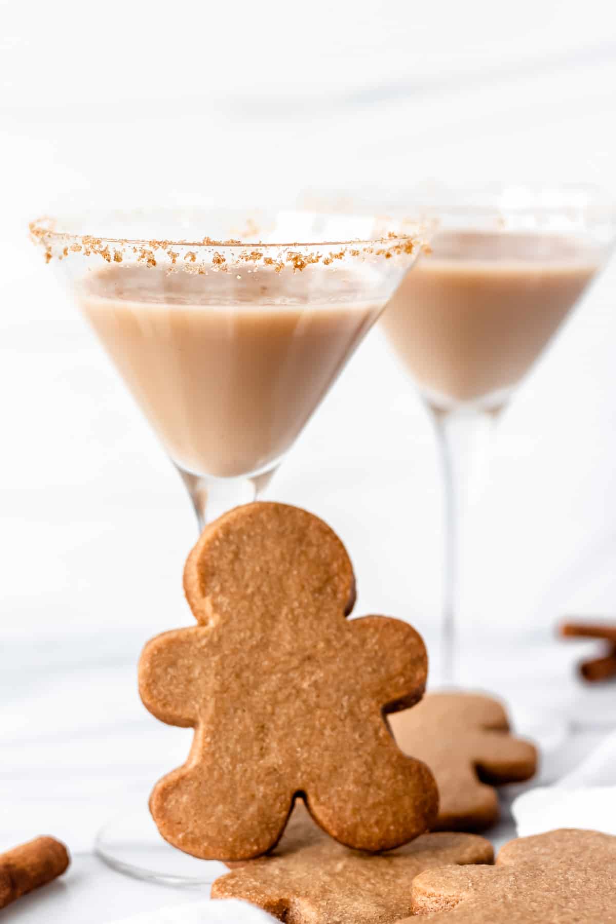 2 Gingerbread martinis with gingerbread man cookies around them with one upright in front of the glass.