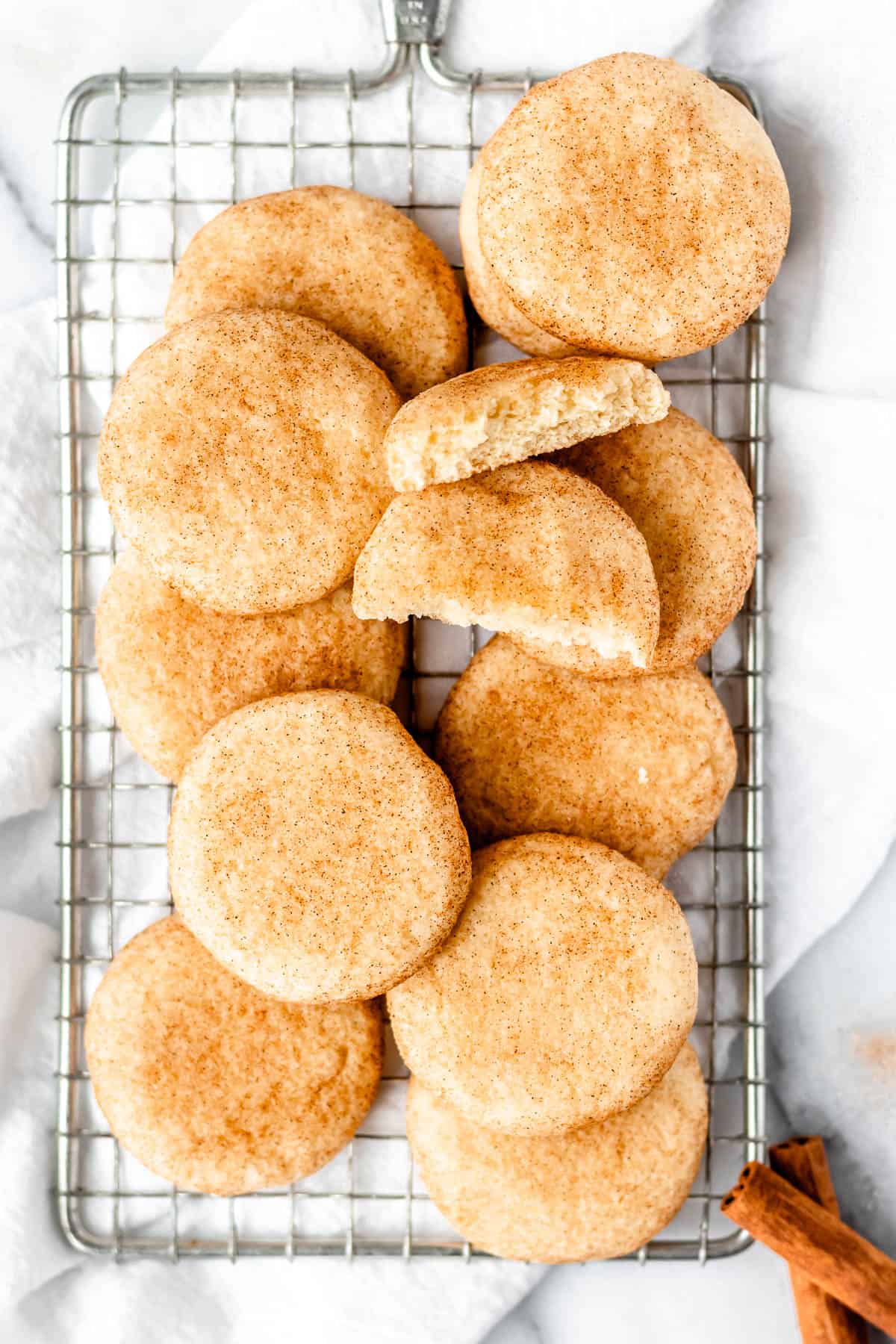 A cooling rack with a bunch of snickerdoodle cookies on it with one cookie broken in half to show the thickness and texture.