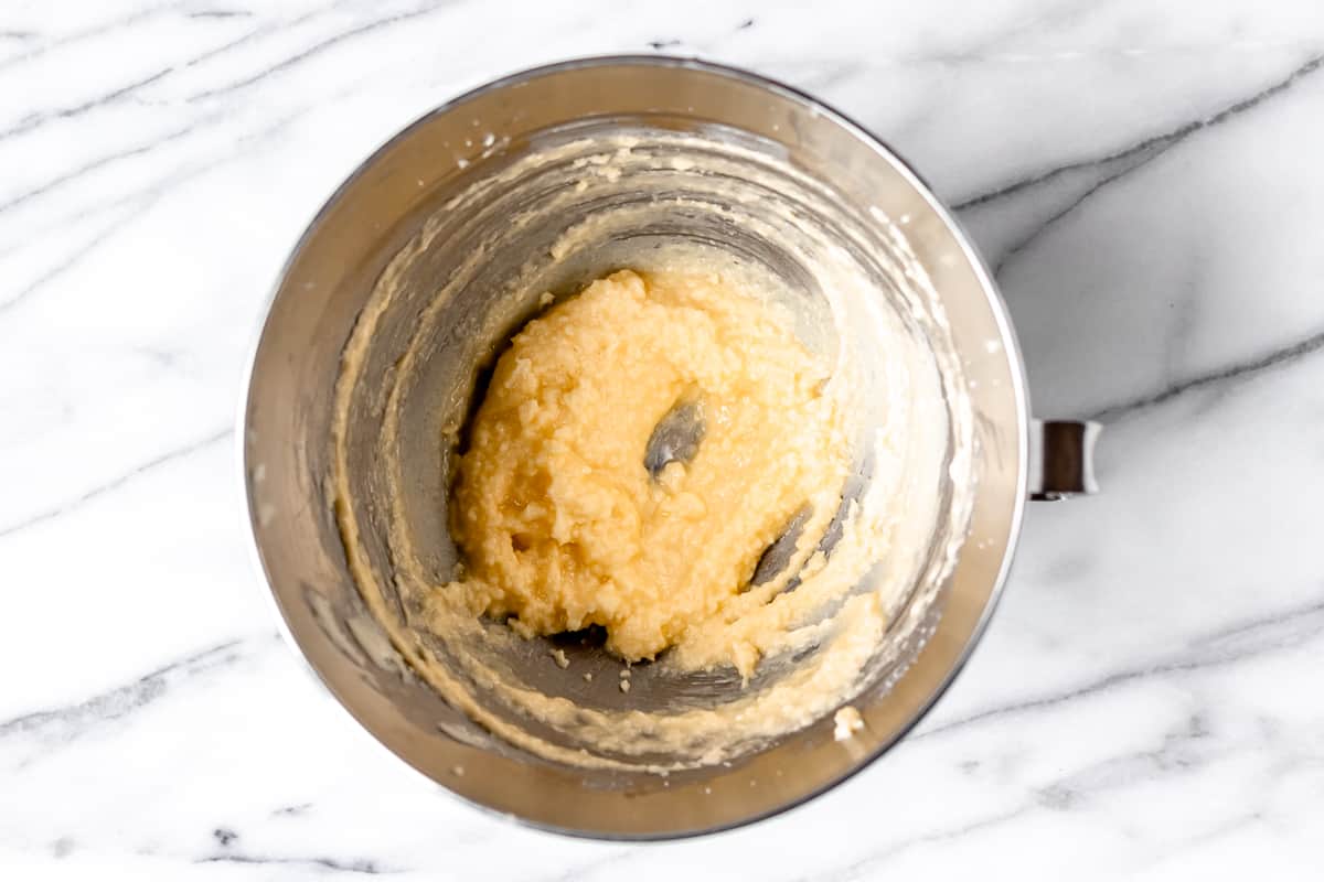 Butter, sugar, egg and vanilla combined in a silver mixing bowl over a marble background.