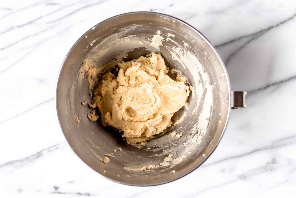 Sugar cookie dough in a silver mixing bowl over a marble background.