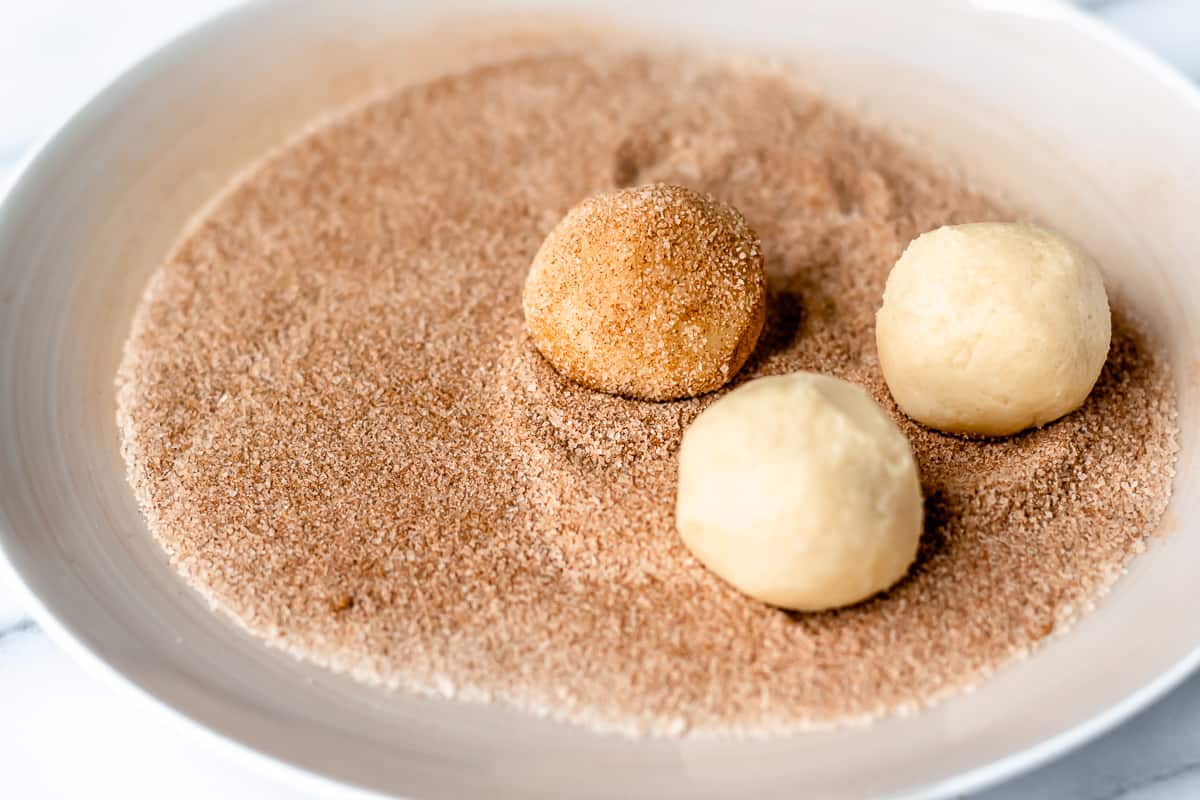 3 dough balls on a plate of cinnamon and sugar with one coated in the mixture.