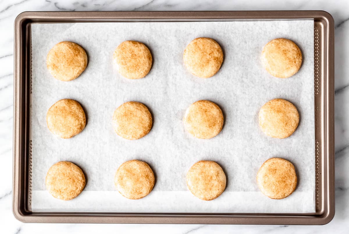 Baked snickerdoodle cookies on a parchment paper lined baking sheet.