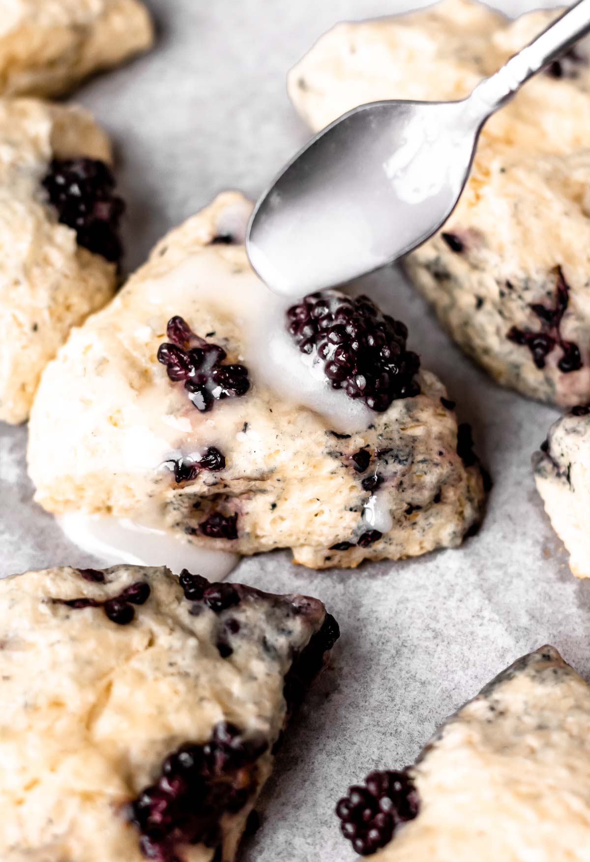 Blackberry scones being drizzled with vanilla glaze.