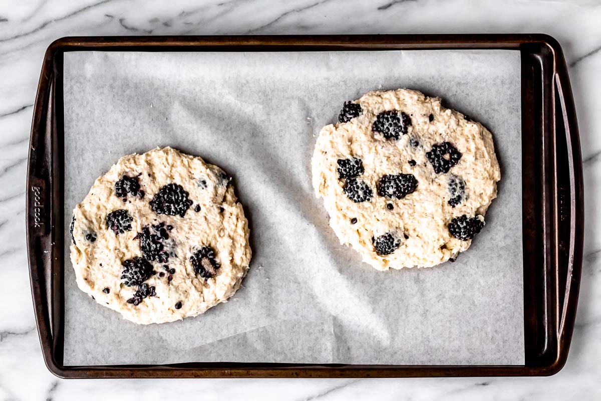 Two scones disks on a parchment paper lined baking sheet.