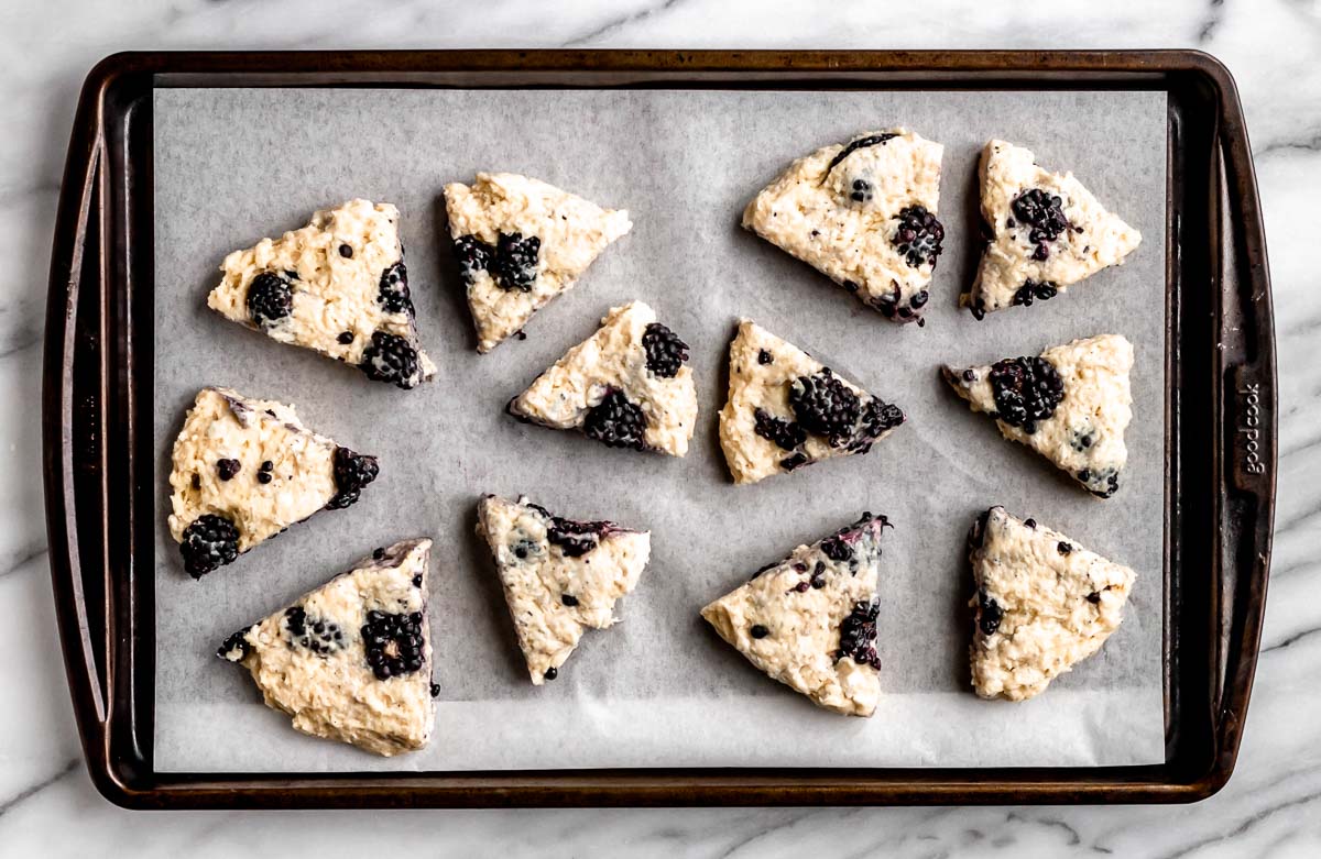 12 baked blackberry scones on a parchment paper lined baking sheet.