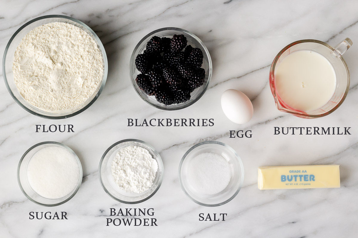 Ingredients needed to make blackberry scones on a marble background with text overlay.