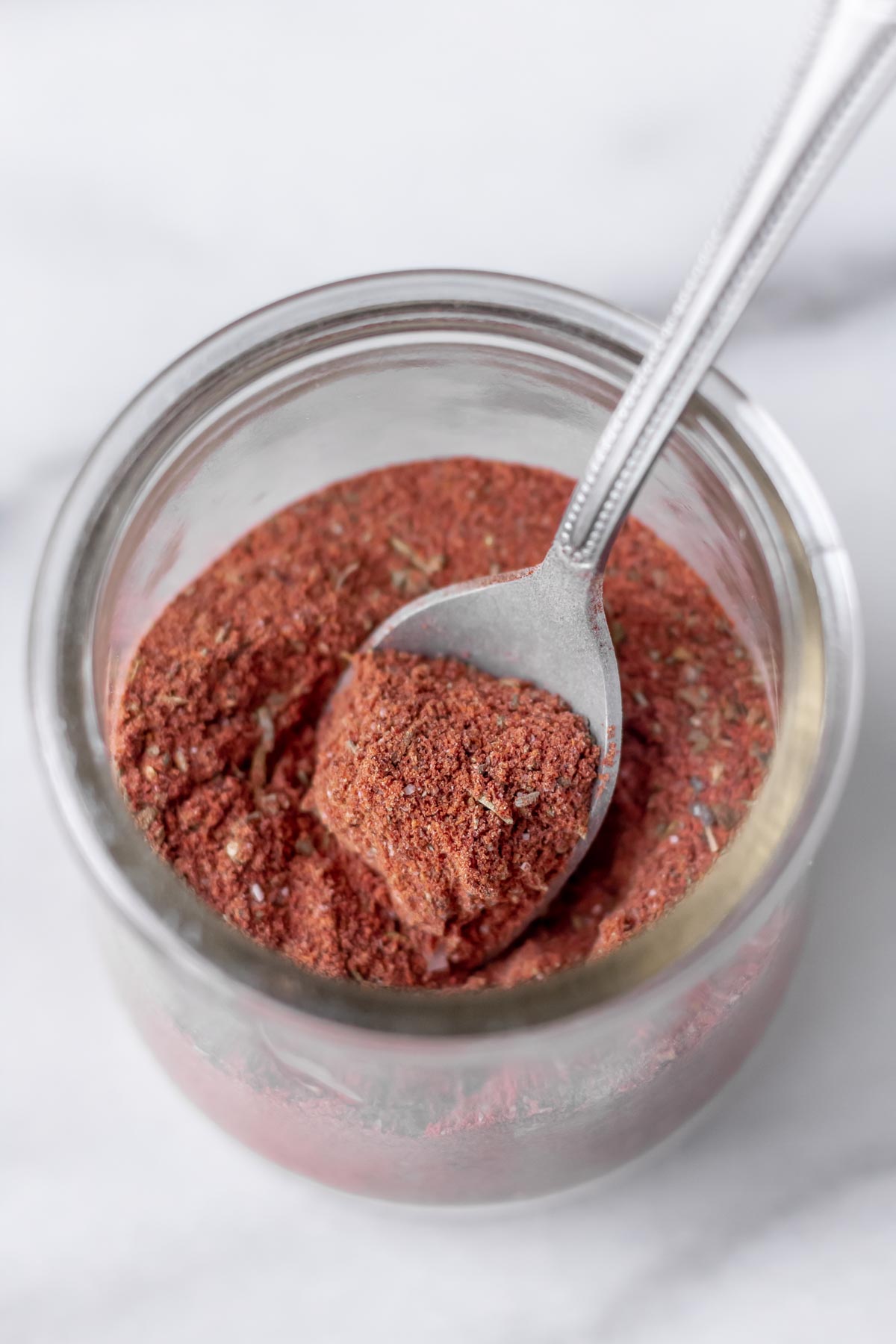 A glass jar filled with blackening seasoning with a small spoon in it.