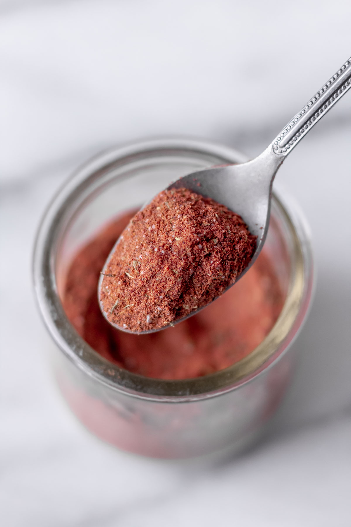 A spoonful of homemade blackening seasoning being lifted up over a jar.