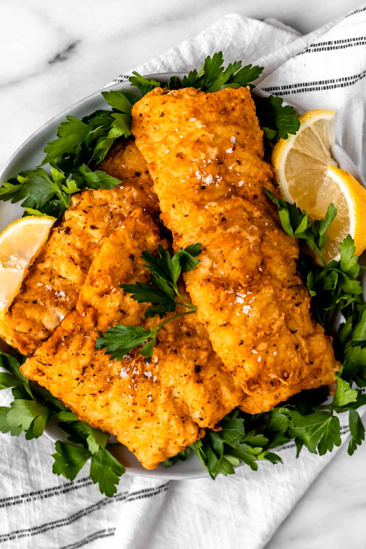 A plate of fried cod fish fillets with parsley and lemon wedges.