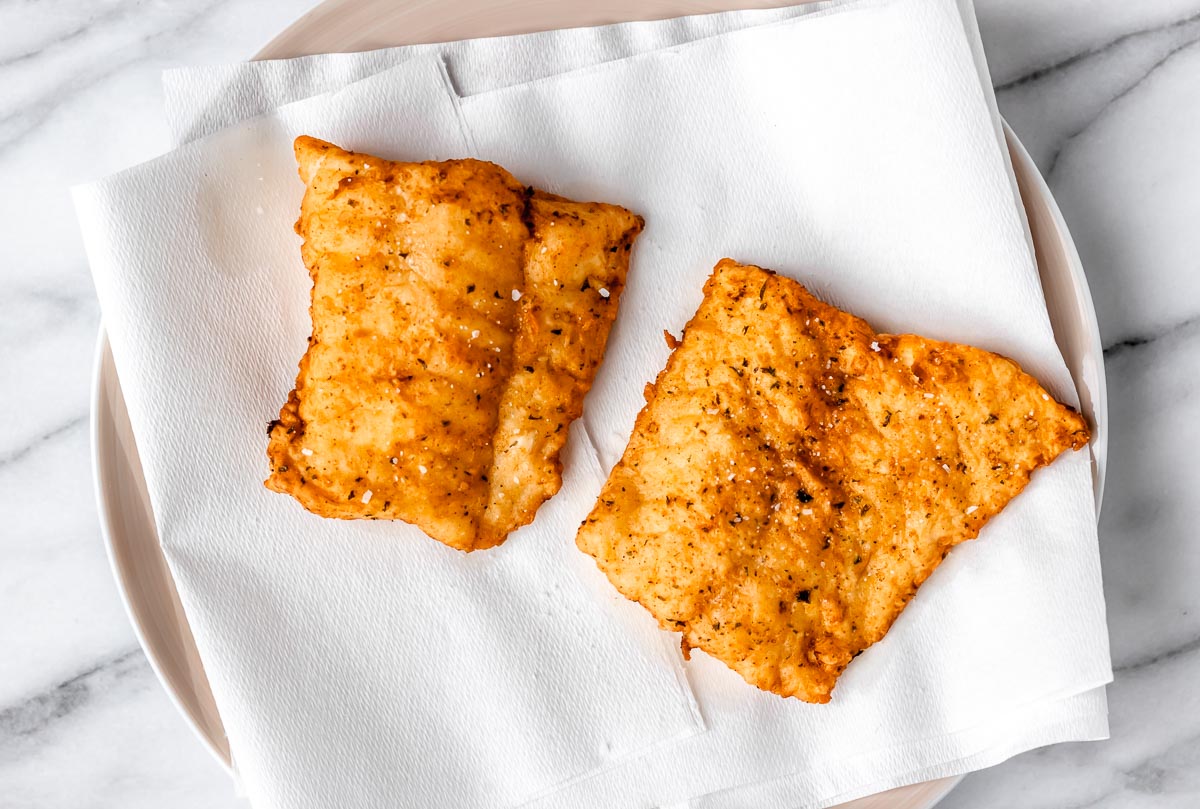 Two fillets of fried cod on a plate lined with paper towels.