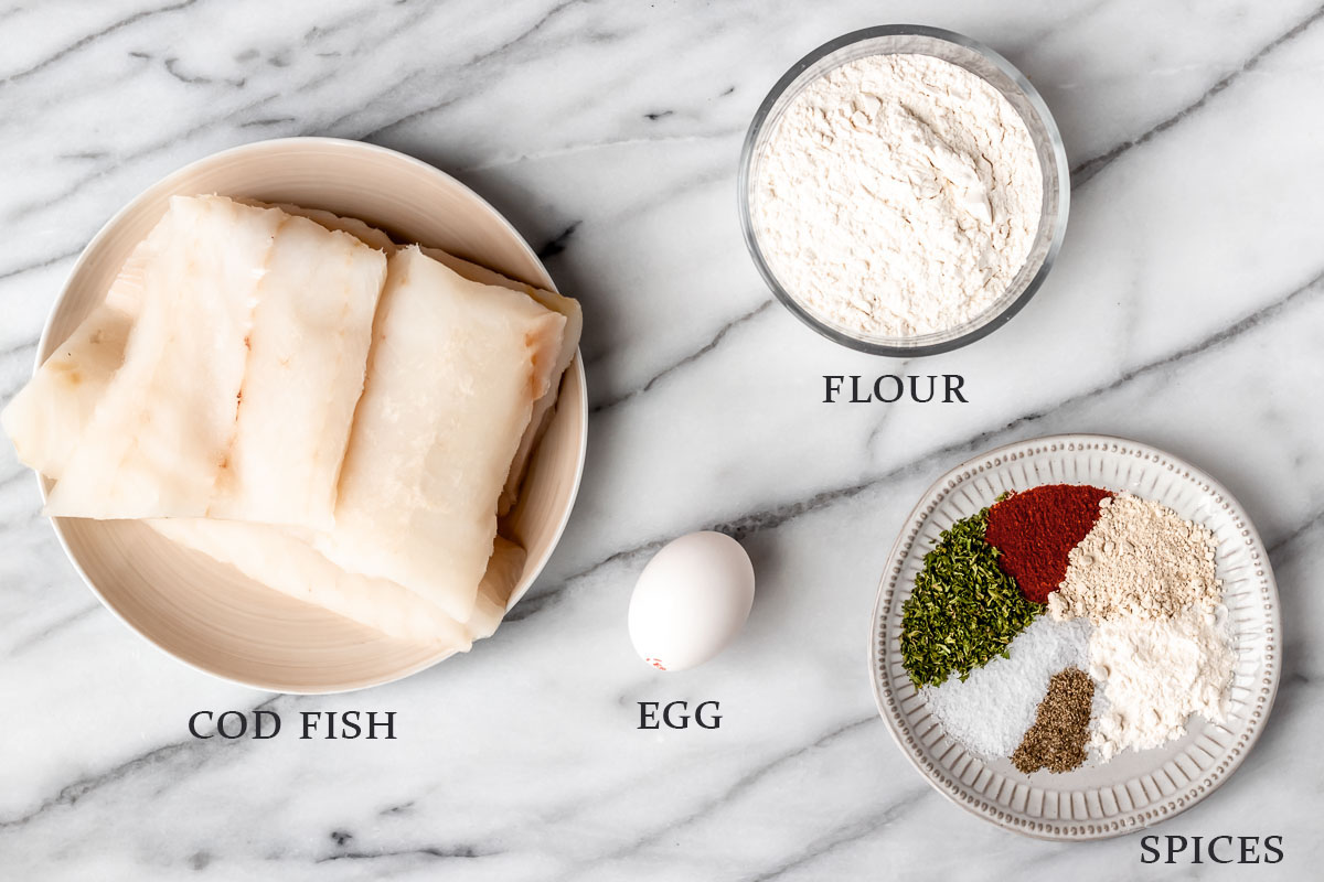 Ingredients needed to make fried cod on a marble background with text overlay.