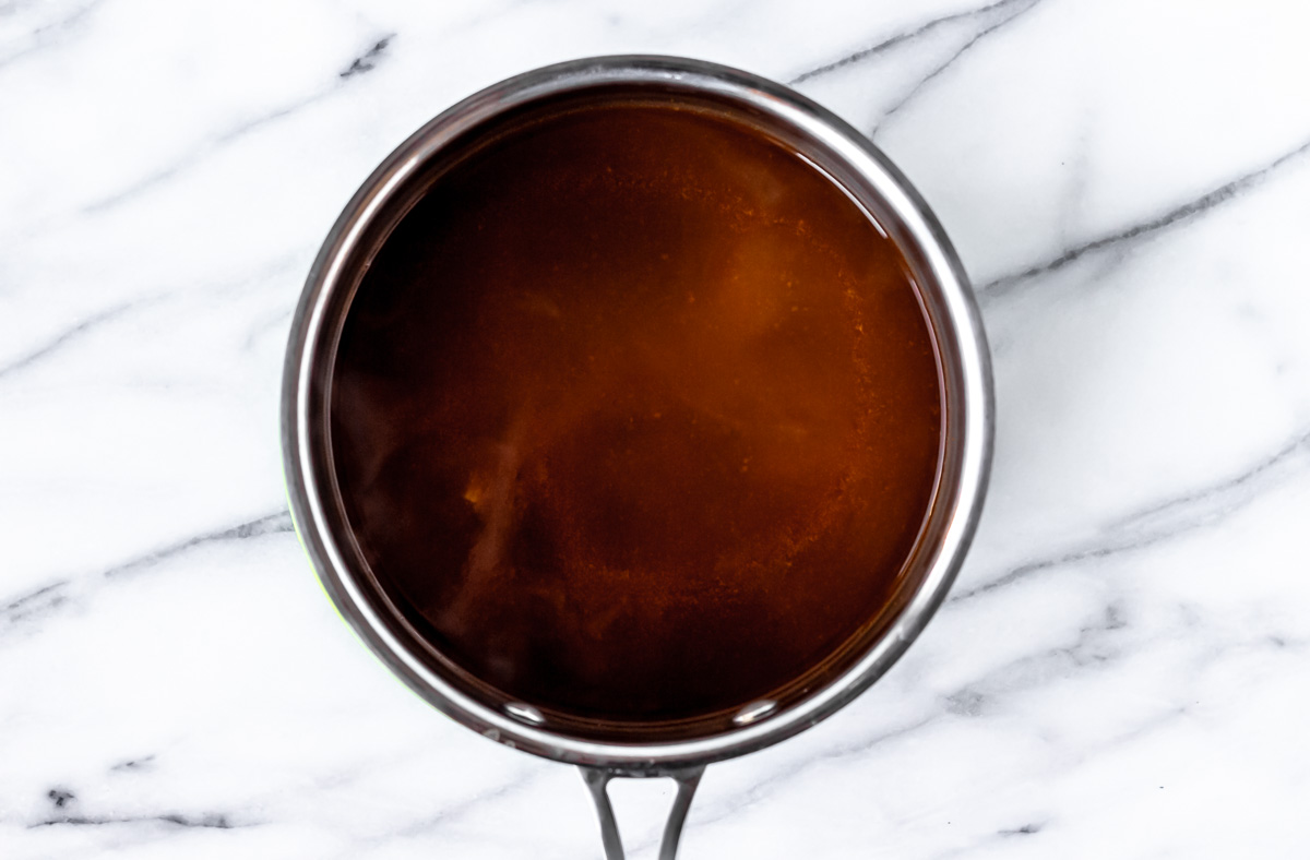 Demi-glace in a silver sauce pot over a marble background.