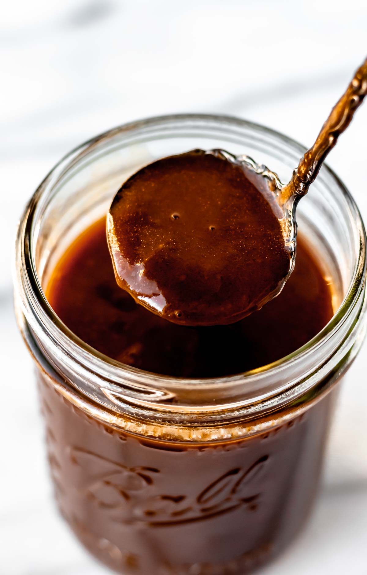 Demi-glace being lifted up with a spoon over a glass jar.