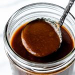 A spoonful of espagnole sauce being lifted up over a canning jar.