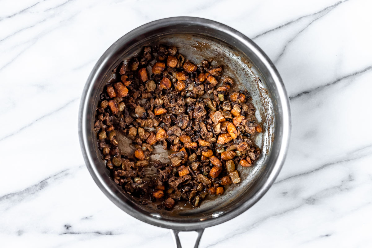 Overhead view of mirepoix vegetables and brown roux in a saucepan.