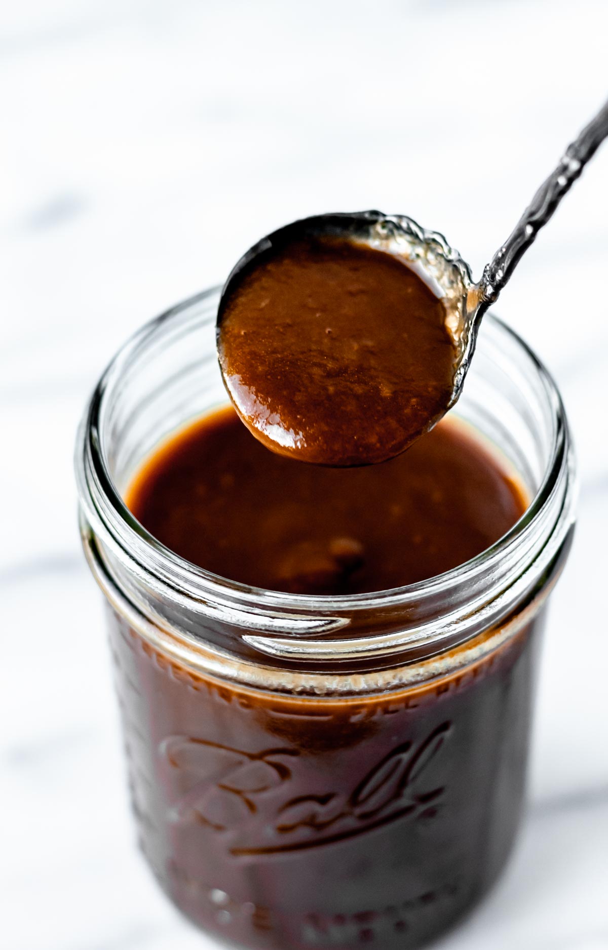 A spoonful of espagnole sauce being lifted up over a canning jar.