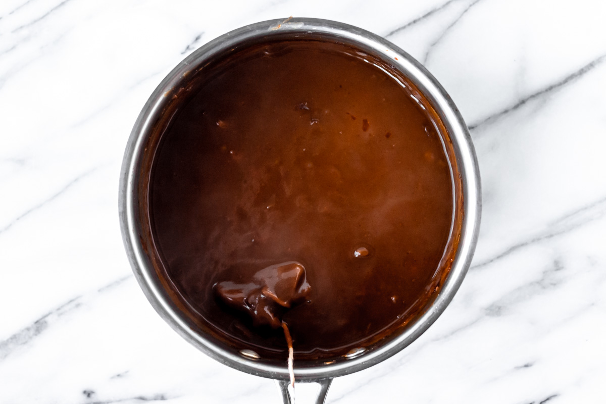 Brown sauce cooking in a saucepan with a sachet in it.