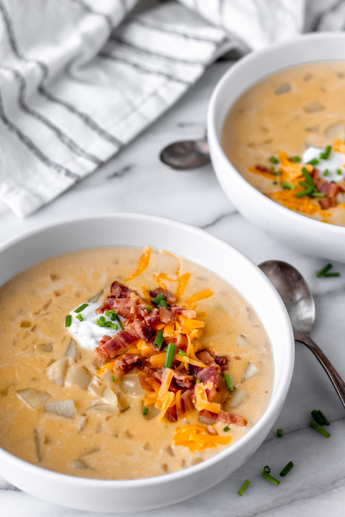 Two bowls of loaded potato soup with spoons and a striped towel near them.