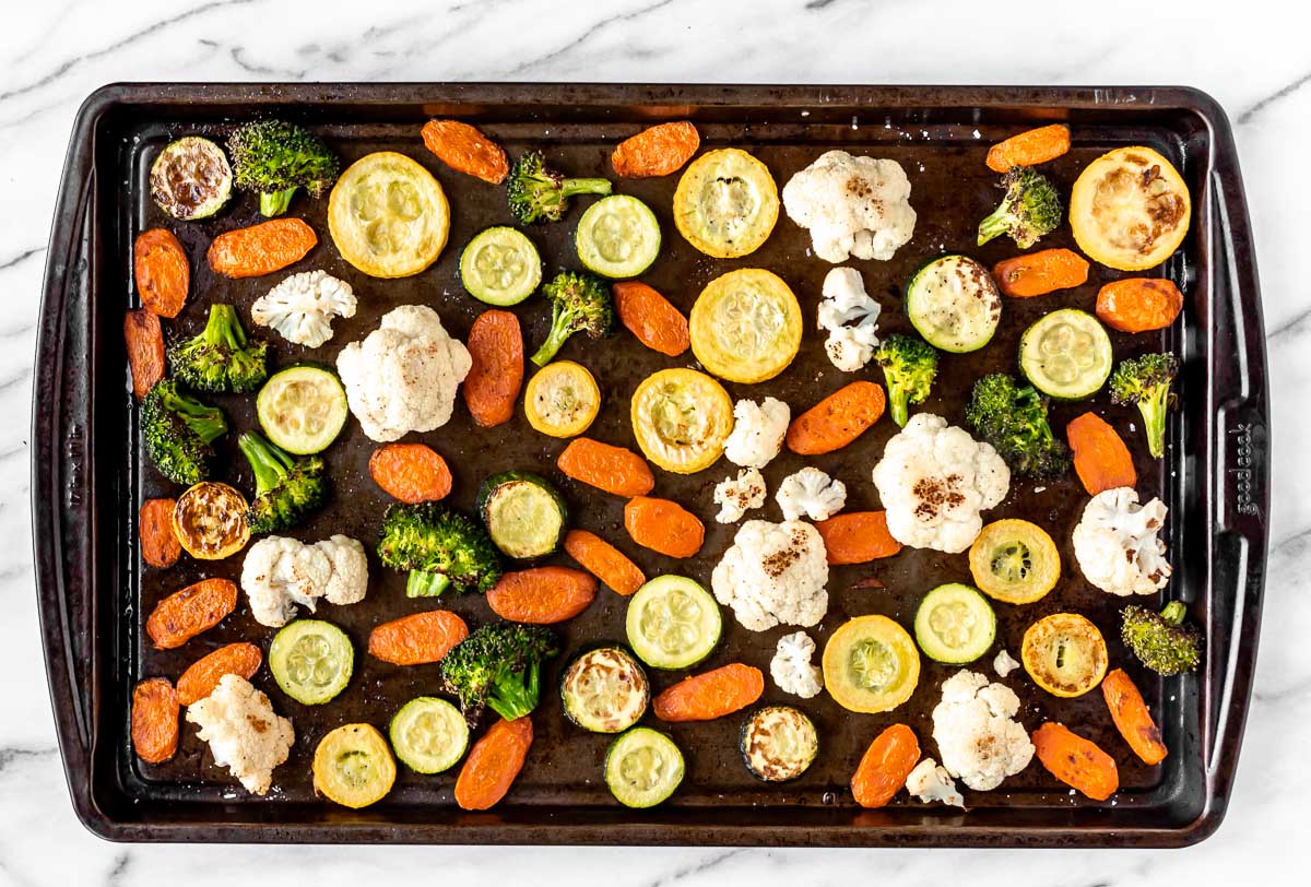 Roasted vegetables spread out onto a sheet pan.