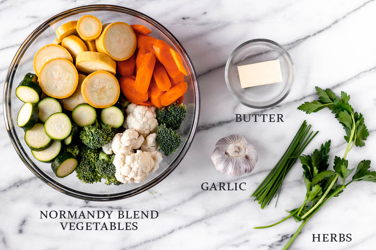 Ingredients needed to make garlic herb normandy blend vegetables on a marble background with text overlay.