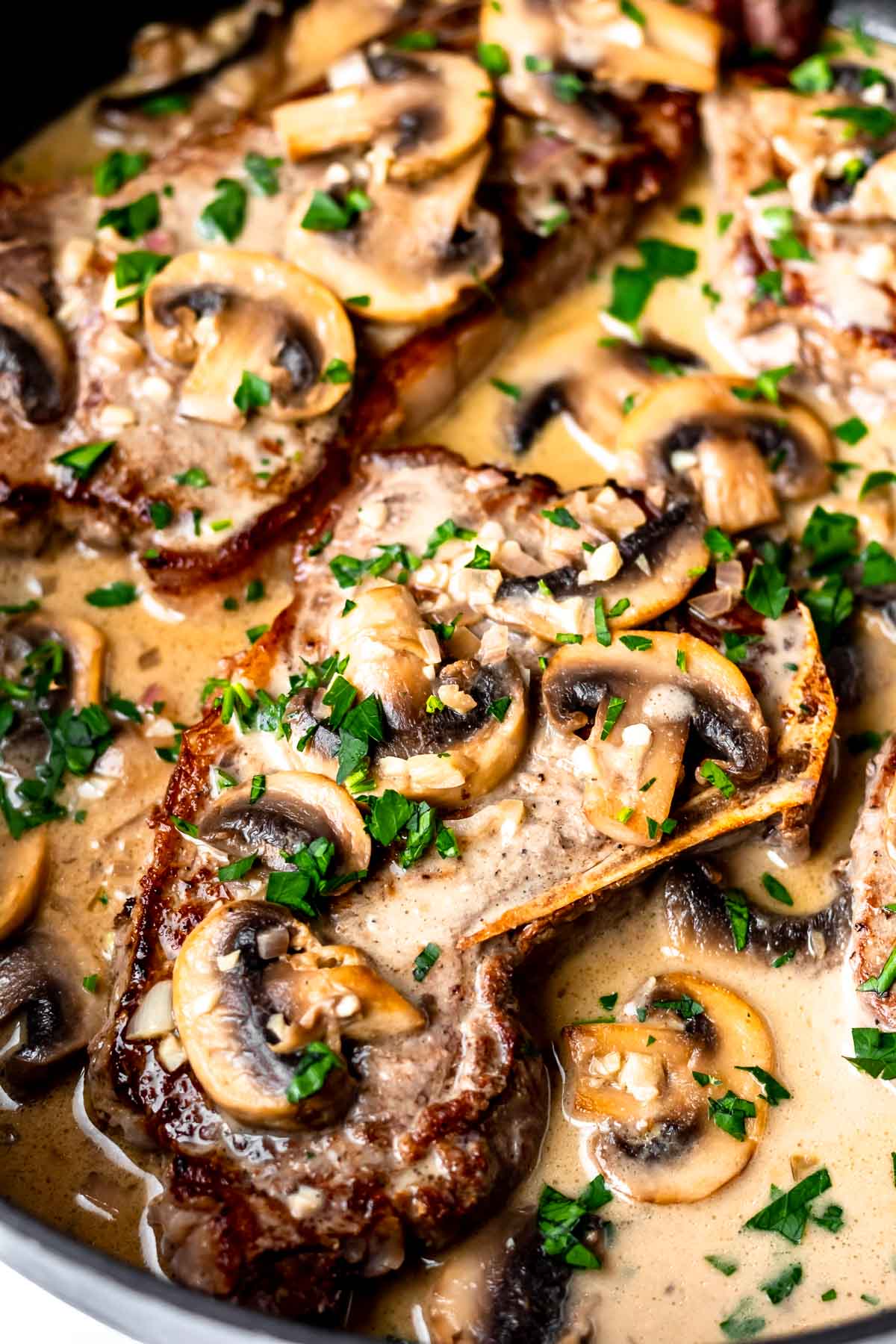 Close up of Steak Diane in a skillet topped with fresh parsley.