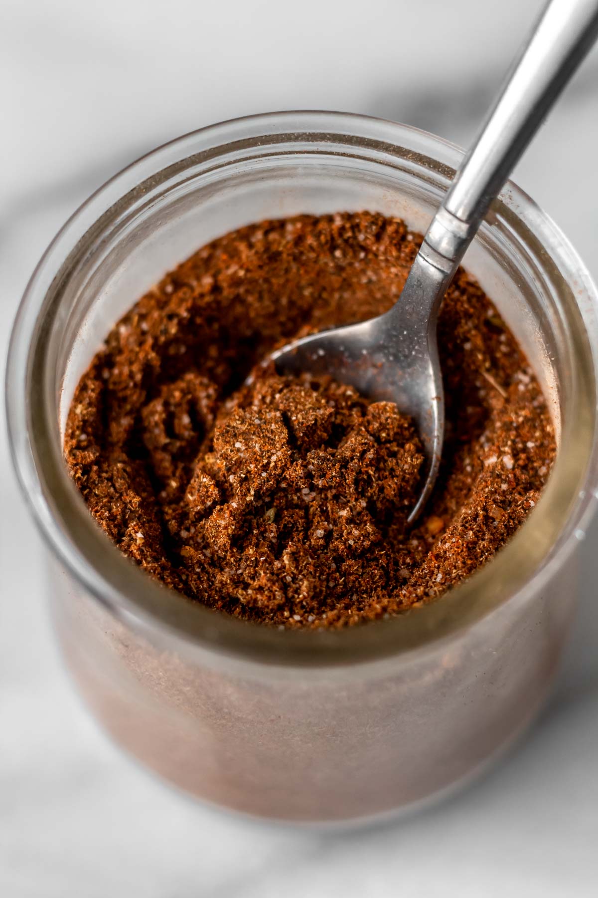 A glass jar of taco seasoning with a small spoon in it.