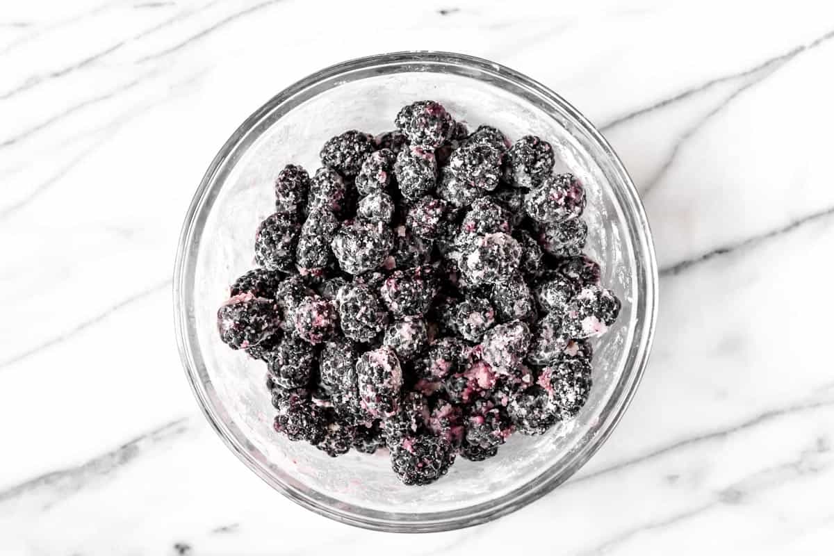 Blackberries tossed with sugar and flour in a glass bowl on a marble backdrop.