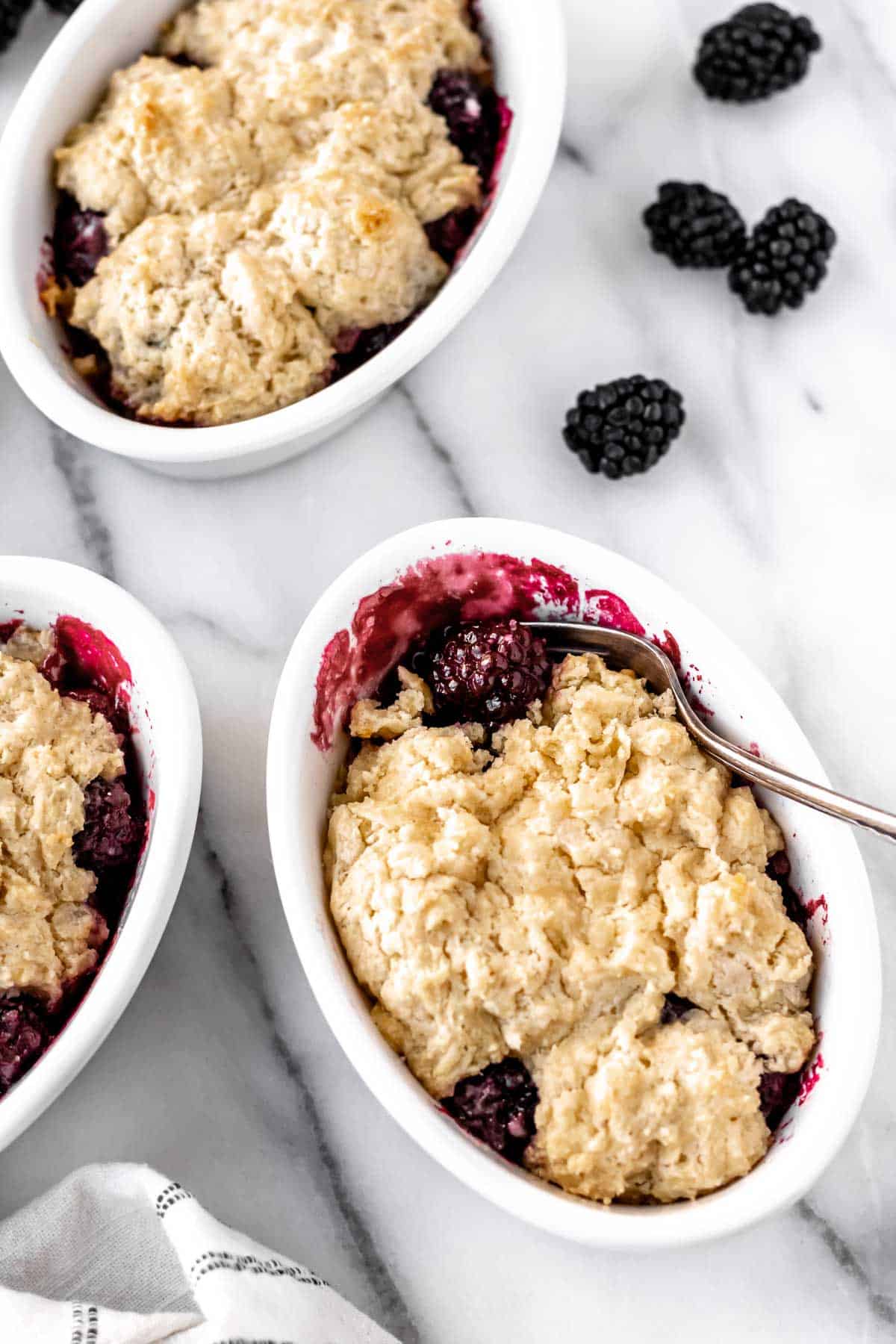 Mini Blackberry Cobbler with a fork in it and some missing with 2 other cobblers partially showing.