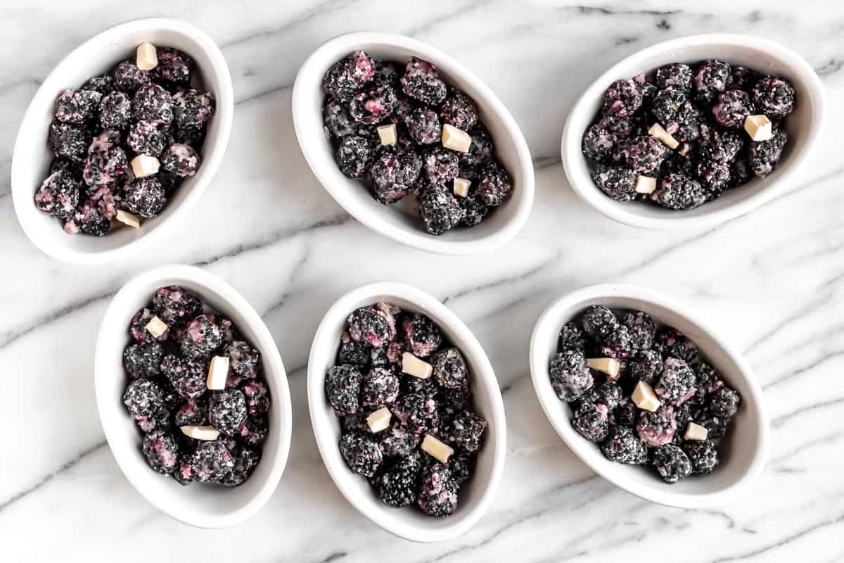 Blackberry filling dotted with butter in 6 individual baking dishes on a marble background.
