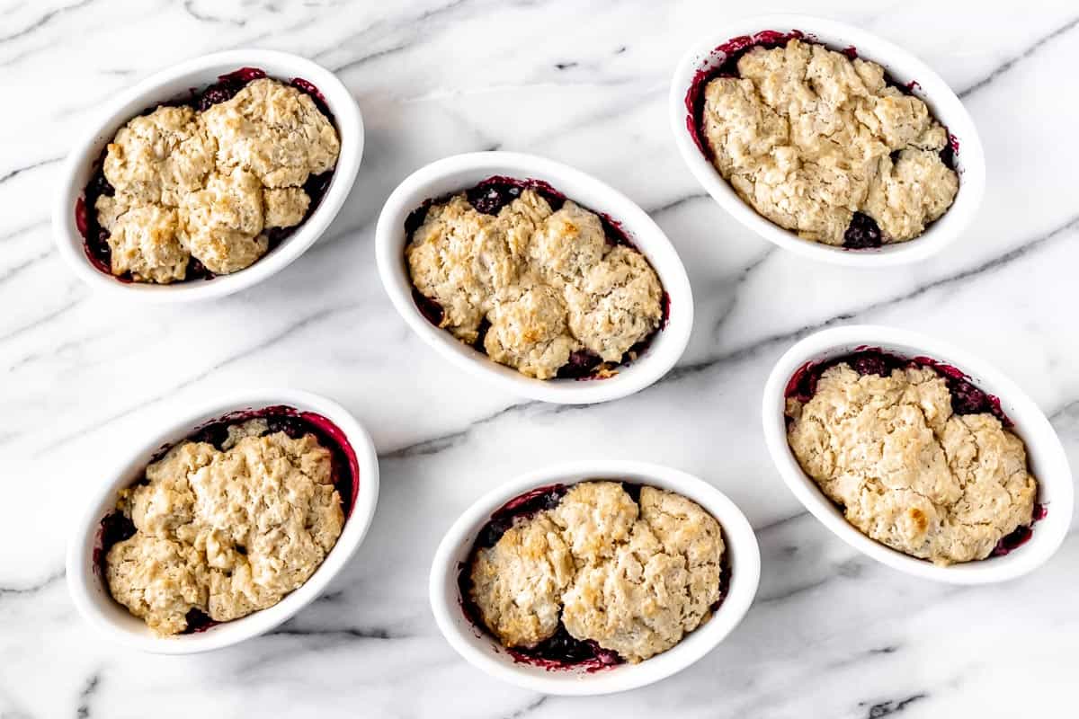 Six baked mini blackberry cobblers on a marble background.