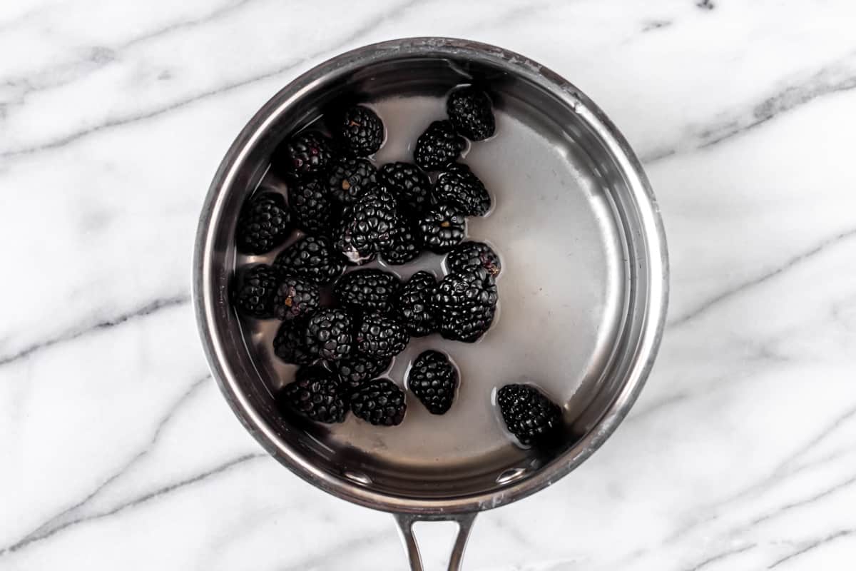 Blackberries, sugar and water in a saucepan on a marble background.